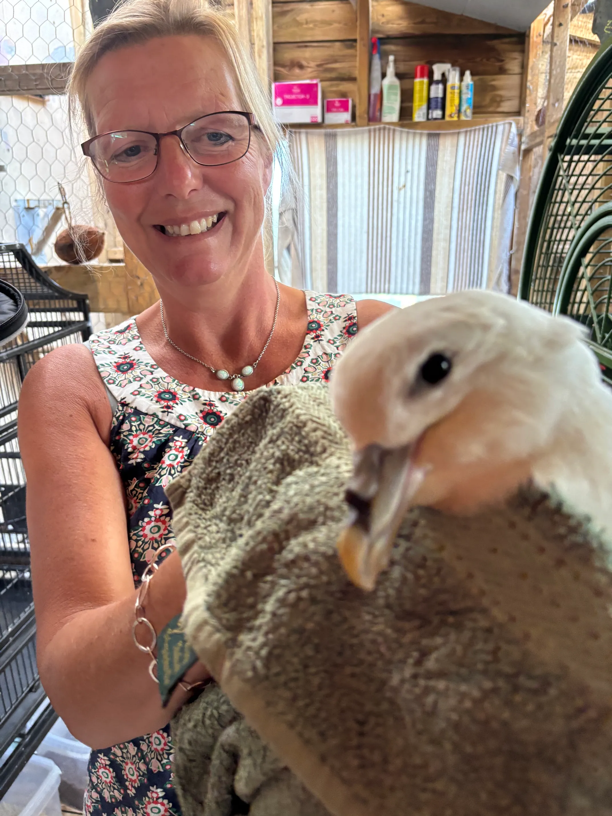 Nikki smiling in a rescue aviary, gently holding a small white bird wrapped in a towel.
